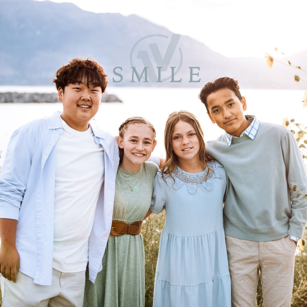 Four One Voice Children's Choir members smiling for a picture in front of a lake with a sunrise and sunflowers in the background.
